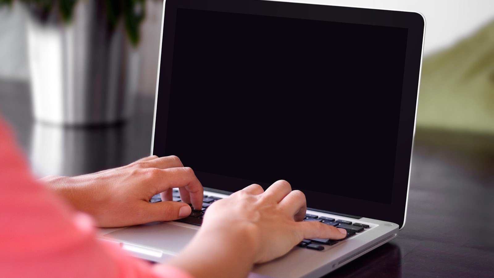 Hands typing on an open laptop keyboard on a wooden desk