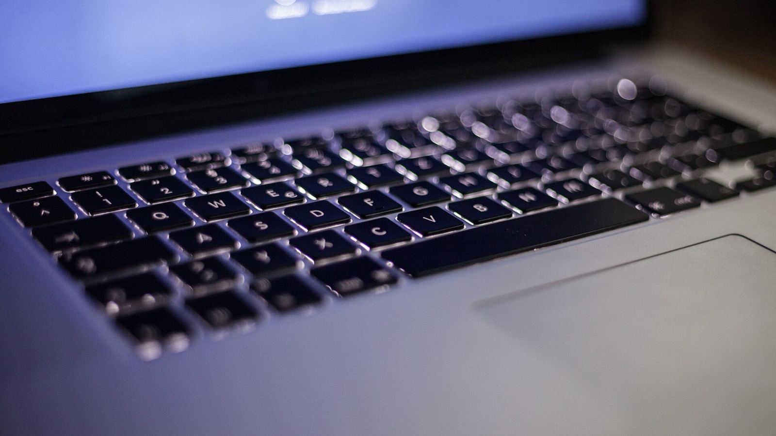 Close-up view of a backlit laptop keyboard in low light