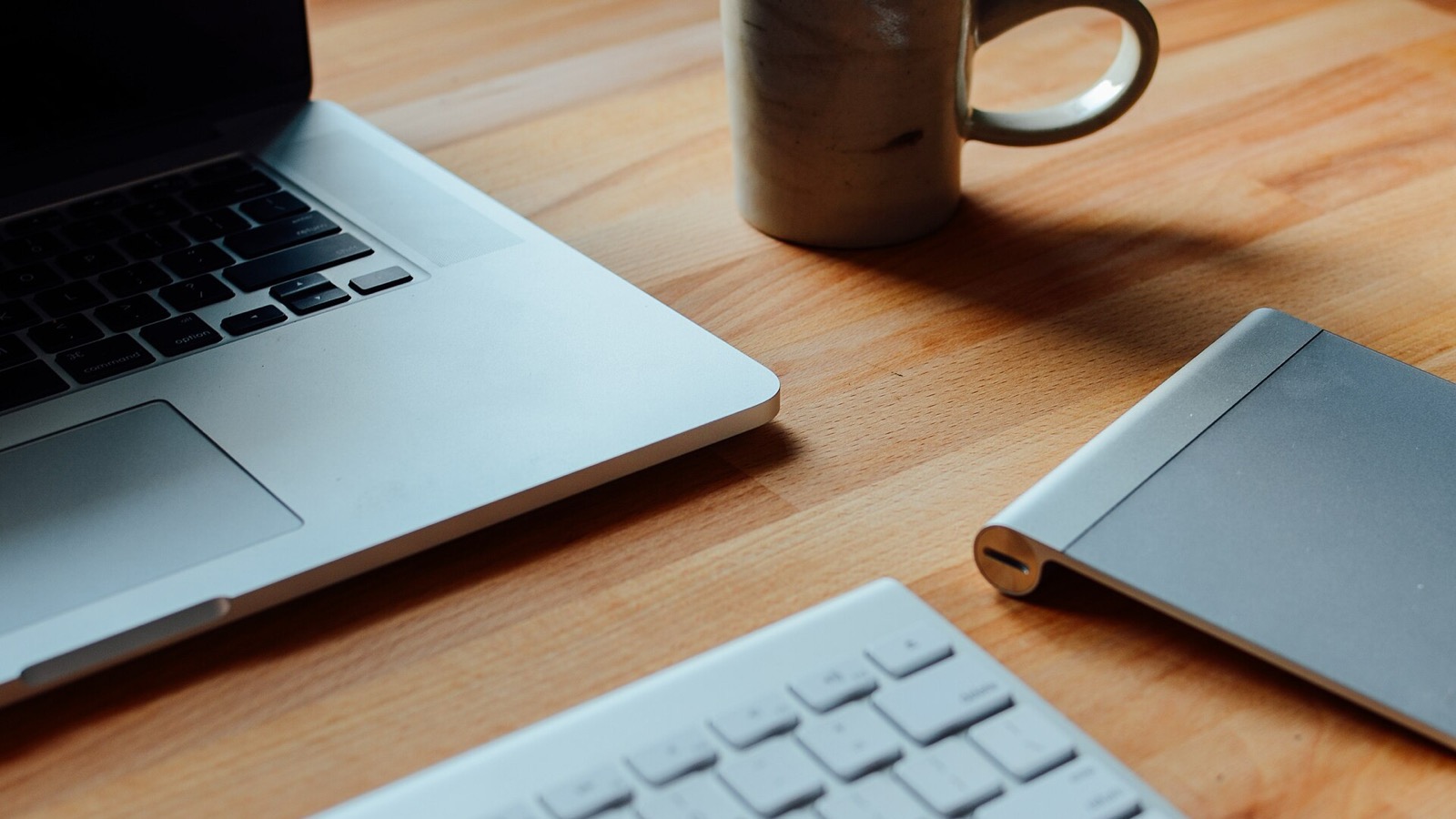 Open laptop beside a ceramic coffee mug on a wooden work table